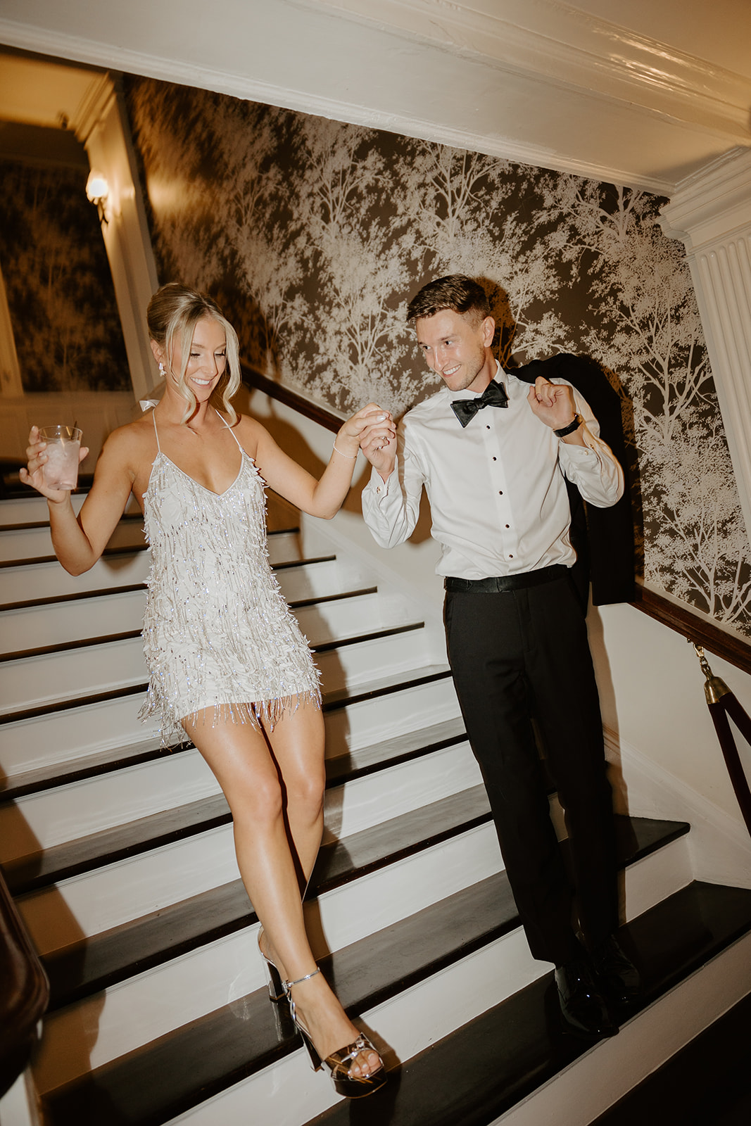 Newlyweds smile as they walk down a grand staircase hand-in-hand, ready for their after-party.